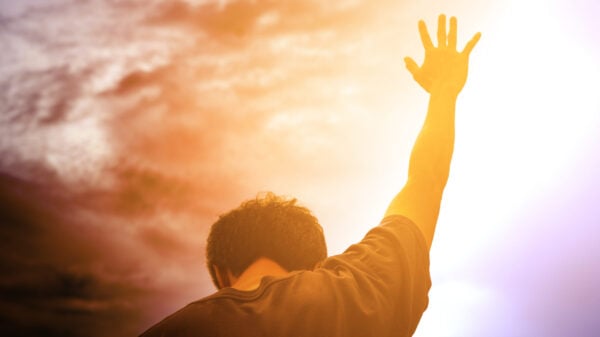 Man reaching toward the sky during sunrise in a moment of prayer and worship