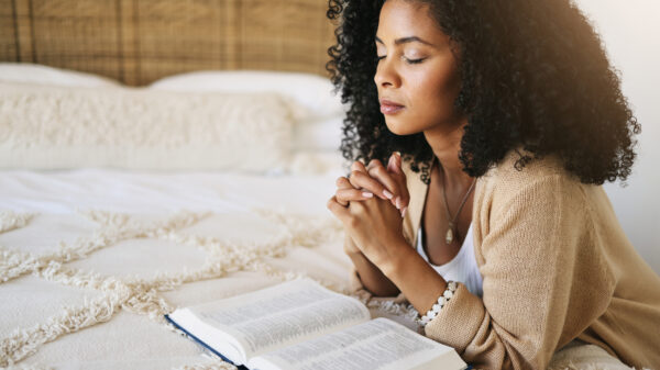 Woman praying quietly on her bed with an open Bible in front of her